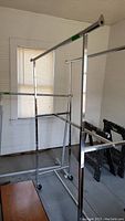 Photo showing two adjustable metal clothing racks side by side, positioned indoors with white walls and a window in the background.