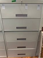 Front view of 5 drawer vertical metal filing cabinet with key showing recessed handles and locking mechanism.