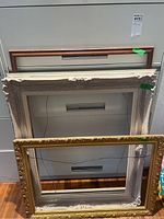 Photo showing three picture frames stacked together: gold ornate frame, white/beige ornate frame, and simpler narrow copper frame