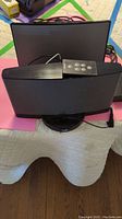 Pair of black Bose speakers, one with iPhone dock, and Bose remote control placed atop speaker. Cables attached and visible.