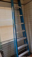 Full view of the blue and aluminum Werner 8-foot fiberglass ladder placed indoors near a window.