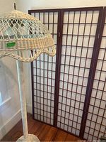 Floor lamp with painted wicker open lattice design and wood and rice paper room divider screen behind it.