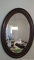 Full view of the vintage oval wall mirror with dark wood frame hanging on a wall, showing overall size and condition.