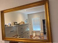 Mirror hanging on a wall reflecting a room with filing cabinets, window, and various items.