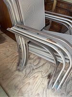 Photo showing stacked metal frame patio chairs with mesh seats and backs, visible rust and oxidation on frames