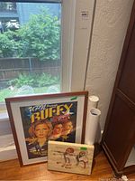 Framed Buffy the Vampire Slayer poster leaning against a window with a wood carved art piece in front