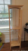 Front view of the wooden tall side tower shelf with three shelves showing natural wood finish and window background.