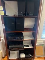 Shelf with Pioneer and JVC speakers on top shelves and Pioneer audio components below, including cassette deck, receiver, CD player with CD magazine, and remotes on bottom shelf.