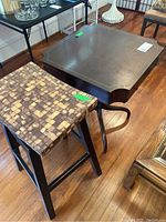 Bar stool next to the pedestal side table on a hardwood floor showcasing seat pattern and table design.