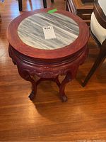 Full view of round side table showing marble look inset top and carved wooden legs.