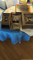 Photo of two vintage folding cameras on a blue cloth with black leather case in the center