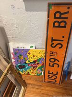 Photo of two abstract paintings leaning against a wall with the street sign standing upright
