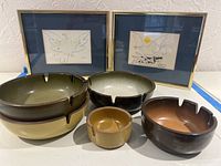 Photo of five ashtrays in earth tone glazes alongside two framed bird art prints on blue mats
