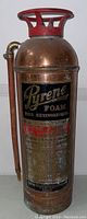 Full front view of copper cylinder showing black and gold Pyrene logo, red top handle and attached hose