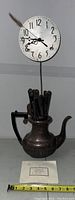 Full view of clock mounted on rod extending from a silver plated teapot base with utensils inside.