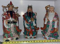 Front view of three large Chinese porcelain figurines with hand-painted floral robes and symbolic items