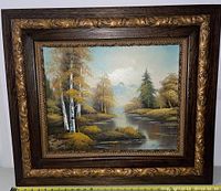 Full view of the oil painting showing a river landscape with trees and mountains, framed with a dark wooden frame with ornate gold carved details on the inner edge.