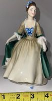 Front view of Royal Doulton Elegance porcelain figurine, seated woman in period dress, showing detailed face, blue bow on bodice, and green cloak.