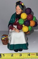 Front view of Royal Doulton Balloon Seller figurine seated holding colorful balloons, measuring roughly 5 inches.