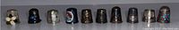 Wide shot showing all ten assorted vintage thimbles in a row, varying in materials and decoration.