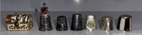 Seven assorted metal thimbles lined side-by-side showing size and style variation