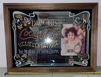 Full front view of vintage Coca Cola mirror showing advertising text and the illustrated woman holding a bottle.