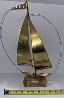 Frontal view of the vintage brass sailboat sculpture showing the two sails, wire rigging detail, and the stone base beneath.