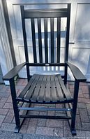 Front view of the black wooden rocking chair showing the slatted seat and backrest and armrests.