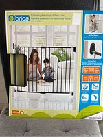 Front of unopened box showing Brica branded extendable metal top of stairs safety gate with photo of woman and child, and size details.
