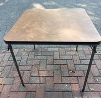 Top view of brown square folding card table with metal legs and rounded corners.