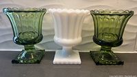 Front view of all three vases: two green glass vases flank one white glass vase, each with a scalloped rim and square footed base.