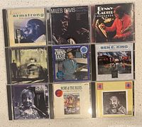 Photo showing nine jazz and blues CDs in jewel cases arranged in three rows of three on a beige surface. Album covers include portraits of Louis Armstrong, Miles Davis, Benny Carter, Count Basie, Ben E. King, Alberta Hunter, and others.
