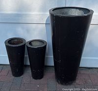 Set of 3 tapered brown metal plant urns standing on brick ground against a white wall showing overall condition with paint chipping and dents.