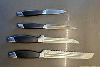 Four knives arranged on a counter showing black handles with metal end caps and different blade types.