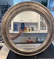 Round wall mirror on a kitchen counter reflecting cabinets and appliances.