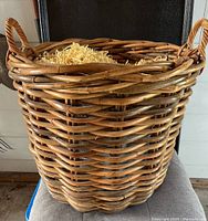 Side view of one large woven wicker basket with handles, showing the tight weave and rustic finish.