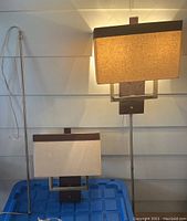 Two wall sconces shown together, one plugged in with visible cord and electrical plug, both with rectangular shades and dark metal frames.