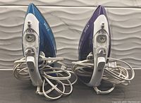 Front view of two T-fal Ultraglide Pro irons showing handles, cords, and control dials; one in blue and one in purple.