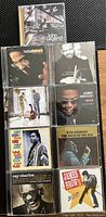 Photo showing a neatly arranged grid of nine male jazz and R&B CDs on black fabric, includes John Legend, Herbie Hancock, Terence Blanchard, Otis Redding, Ray Charles, and James Brown.