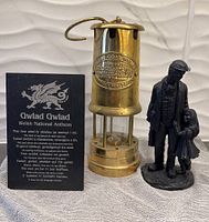 Photo of plaque with Welsh National Anthem text and the brass coal mining lantern and coal miner statue placed next to it.