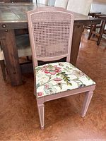 Front view of a hand painted cane-back accent chair with a floral upholstered seat.
