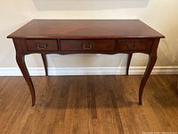 Front view of antique wooden desk showing three drawers and cabriole legs.