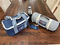 Photo of entire lot including cooler bag, beach mat rolled with strap, portable fan with USB cable, and insulated water bottle on wooden table.