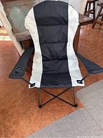 Front view of brand new black and white camping chair with cup holder on right armrest, showing padded fabric seat and back.