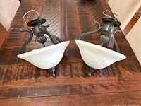 Pair of ceiling mount lights with curved dark metal arms and frosted white glass shades on a wooden table.