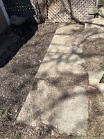 Concrete slabs arranged on the ground showing rectangular and square shapes in outdoor environment with dirt and natural wear.