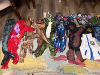 Costumes laid flat on a brown and multicolored rug showing dinosaur costumes, Transformers costumes, ninja costume, Iron Man, Beyblade vest, and Hulk fist glove