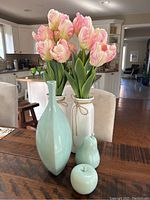 Photo of two vases with artificial pink and white tulips and three small pale blue/green porcelain decorative items on wooden table in kitchen area.