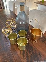 Photo of two gold decorative spheres, three gold planters, one blue glass vase, and one gold hanging planter on a dining table.