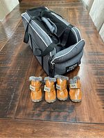 Photo of gray pet carrier with four small brown dog booties lined in front, placed on a wooden surface